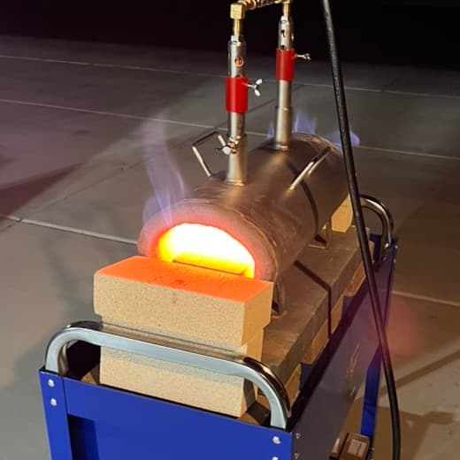 A small gas forge glowing orange on a rolling cart at dusk